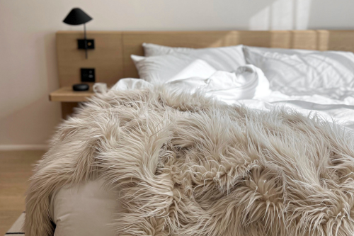 Bed with side table and white sheets, faux fur blanket