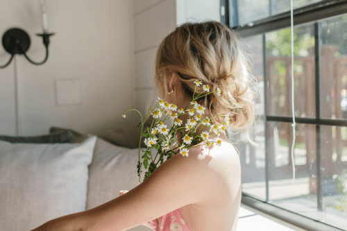 Girl facing away from camera holding flowers with hair in a messy bun