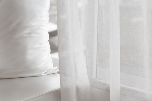 white drapes covering a window with a white bench and pillow in the corner