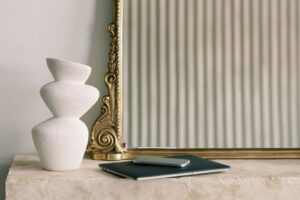 white ceramic vase and folder on a marble stand with a golden mirror.